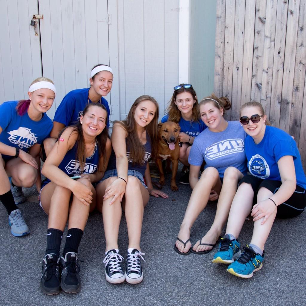 a group of students pose outside in matching blue u n e t-shirts with a dog