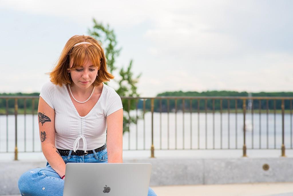 一个学生坐在水边的长凳上用笔记本电脑工作