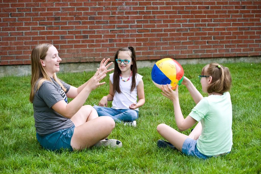 A special education student throws a beach ball outside with two elementary school children