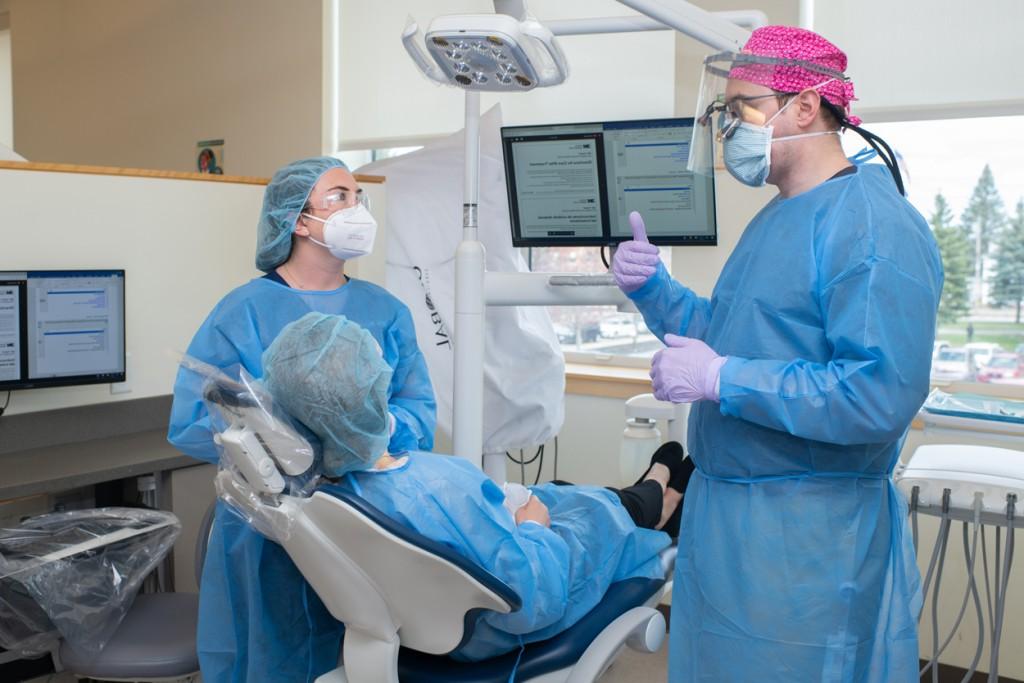 一名牙科学生和一名穿着蓝色手术服的医学院学生与一名病人讨论牙科工作