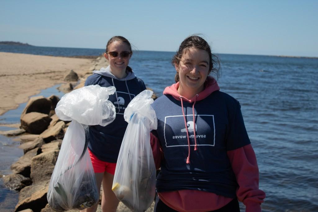 Two students hold up trash bags as they clean up a beach