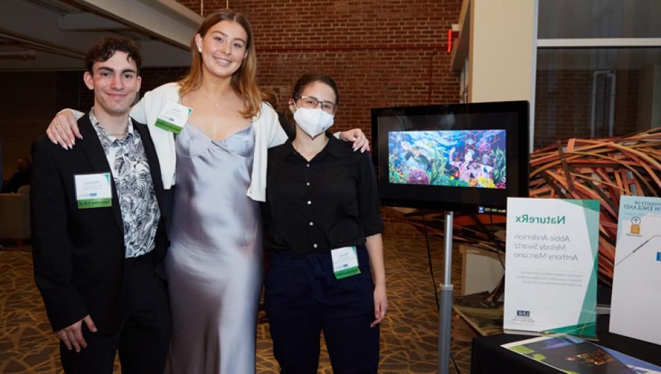 Three U N E students standing by their project at the 2022 Innovation Showcase