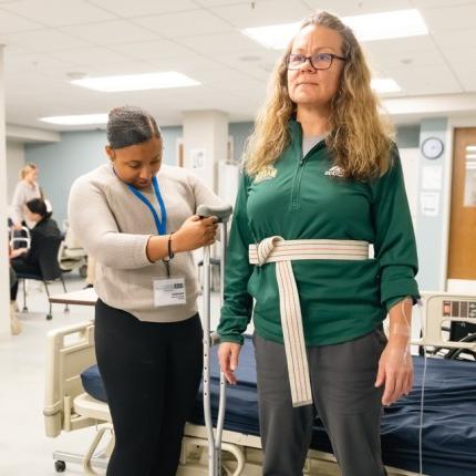 一名体育专业的学生在为病人练习测量拐杖