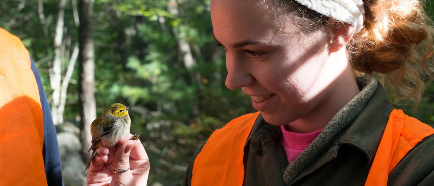 A female student looks at a small bird perched on her hand