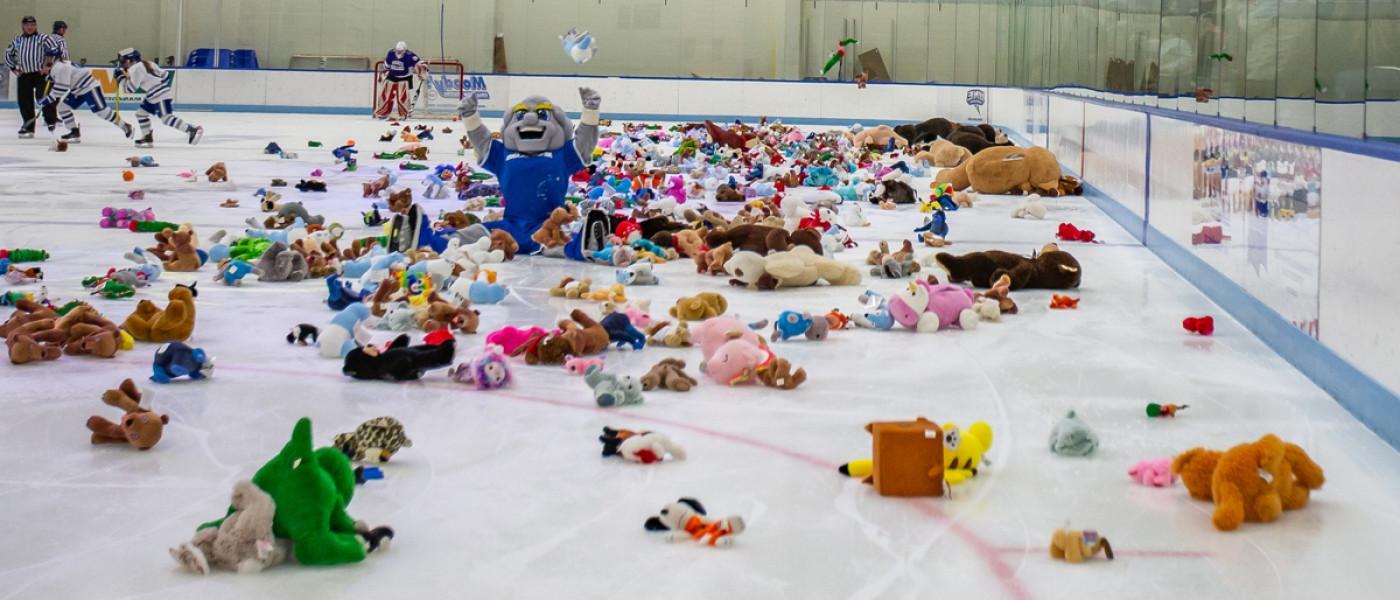 U N E mascot Stormin' Norman sits on the ice of a honkey rink surrounded by stuffed animals for a Teddy Bear Toss event