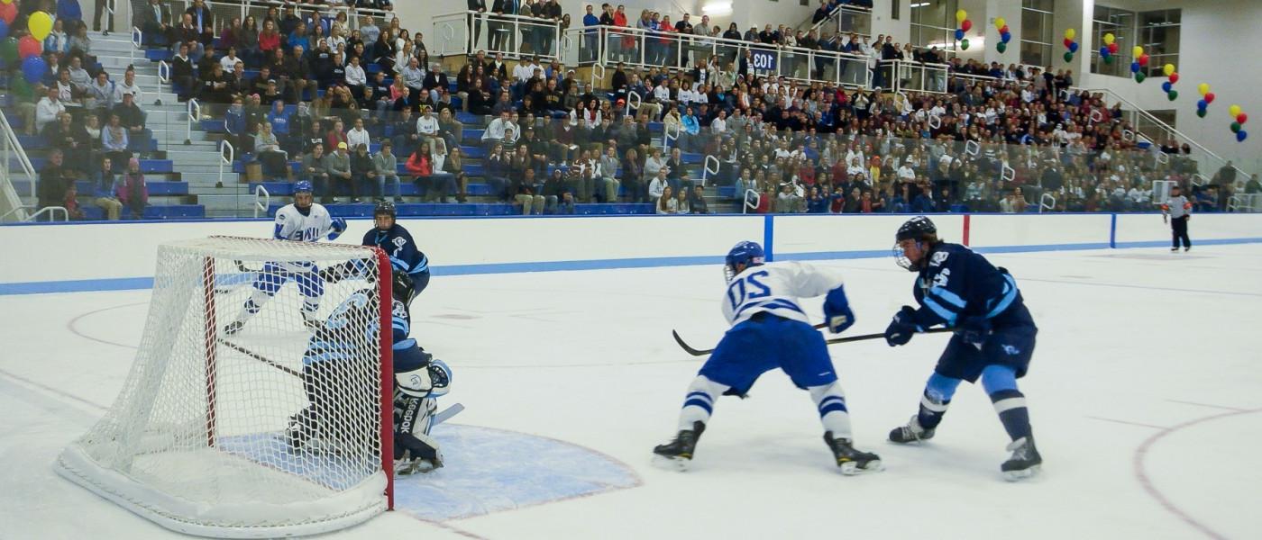 The U N E men's hockey team plays while a large crowd looks on 