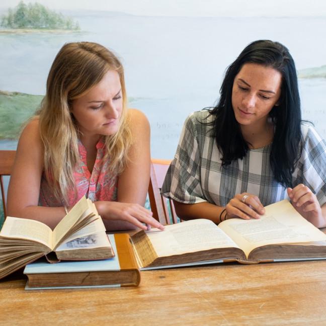 两个学生一起在一张桌子上学习，桌子上有很多书