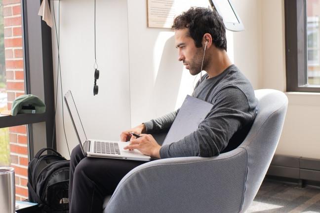 一个学生坐在扶手椅上用笔记本电脑工作