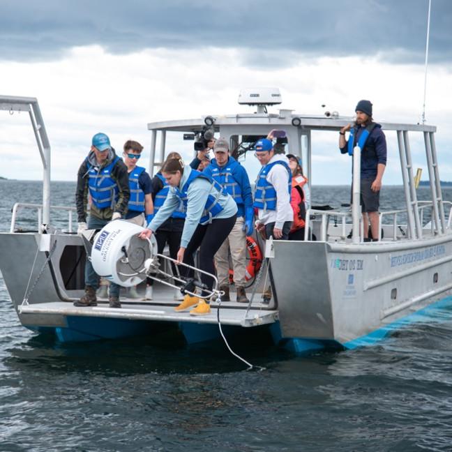 一群学生在一艘欧盟船上从海洋中捡回一个白色的鲨鱼浮标