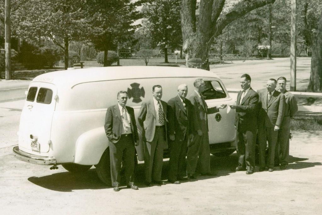 An archival black and white photo of previous C O M students in front of a medical van
