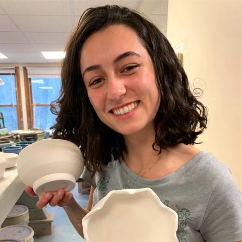 Olivia Scott stands smiling at the camera holding her handmade ceramics